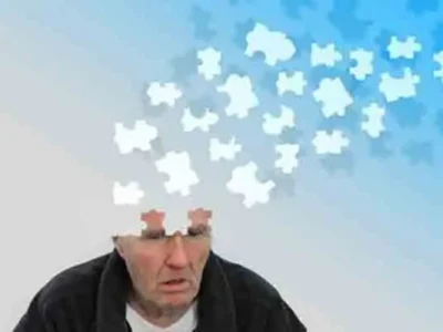 Homem idoso com expressão de preocupação, peças de um quebra-cabeça se dispersam sobre fundo azul, simbolizando a memória e a qualidade de vida na doença de Alzheimer.