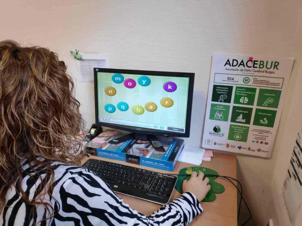 Pessoa sentada em frente a um computador em um escritório, com NeuronUP na tela e documentos sobre a mesa.