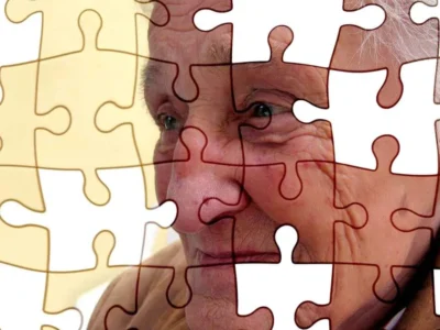 Rosto de uma pessoa idosa parcialmente coberto por peças de quebra-cabeça transparentes, simbolizando a percepção visual na doença de Alzheimer.