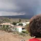 Pessoa de costas com cabelo cacheado observa uma paisagem de La Palma: casas, montanhas e céu nublado em um ambiente árido.