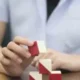 Mão segurando um bloco de brinquedo vermelho e branco enquanto se constrói uma estrutura, em um ambiente de sala de aula.