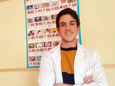 Retrato de José Antonio Silva, fonoaudiólogo, com bata branca ao lado de um cartaz alfabético, premiado por seu trabalho com o NeuronUP.