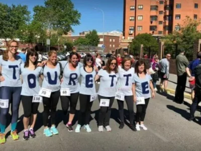 Grupo de mulheres com camisetas TOURETTE e números no peito, em ambiente urbano, mostrando apoio e sensibilização.