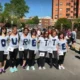 Grupo de mulheres com camisetas TOURETTE e números no peito, em ambiente urbano, mostrando apoio e sensibilização.