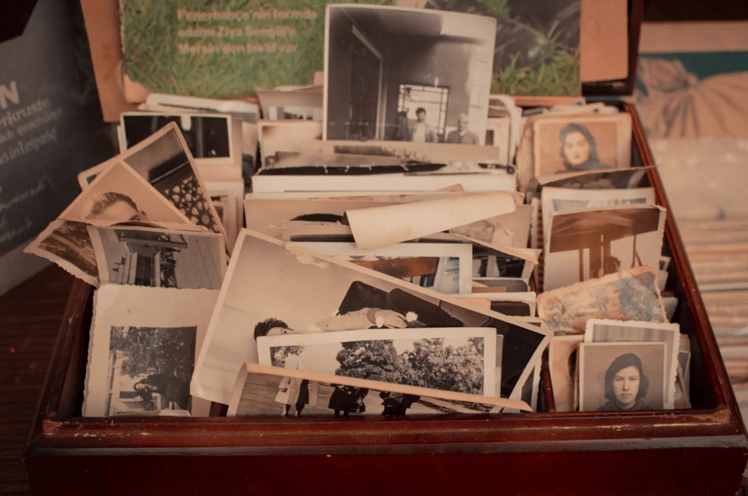 Caixa de madeira com fotos em preto e branco e algumas em cores, empilhadas; rostos e nostalgia que evocam a memória afetiva.