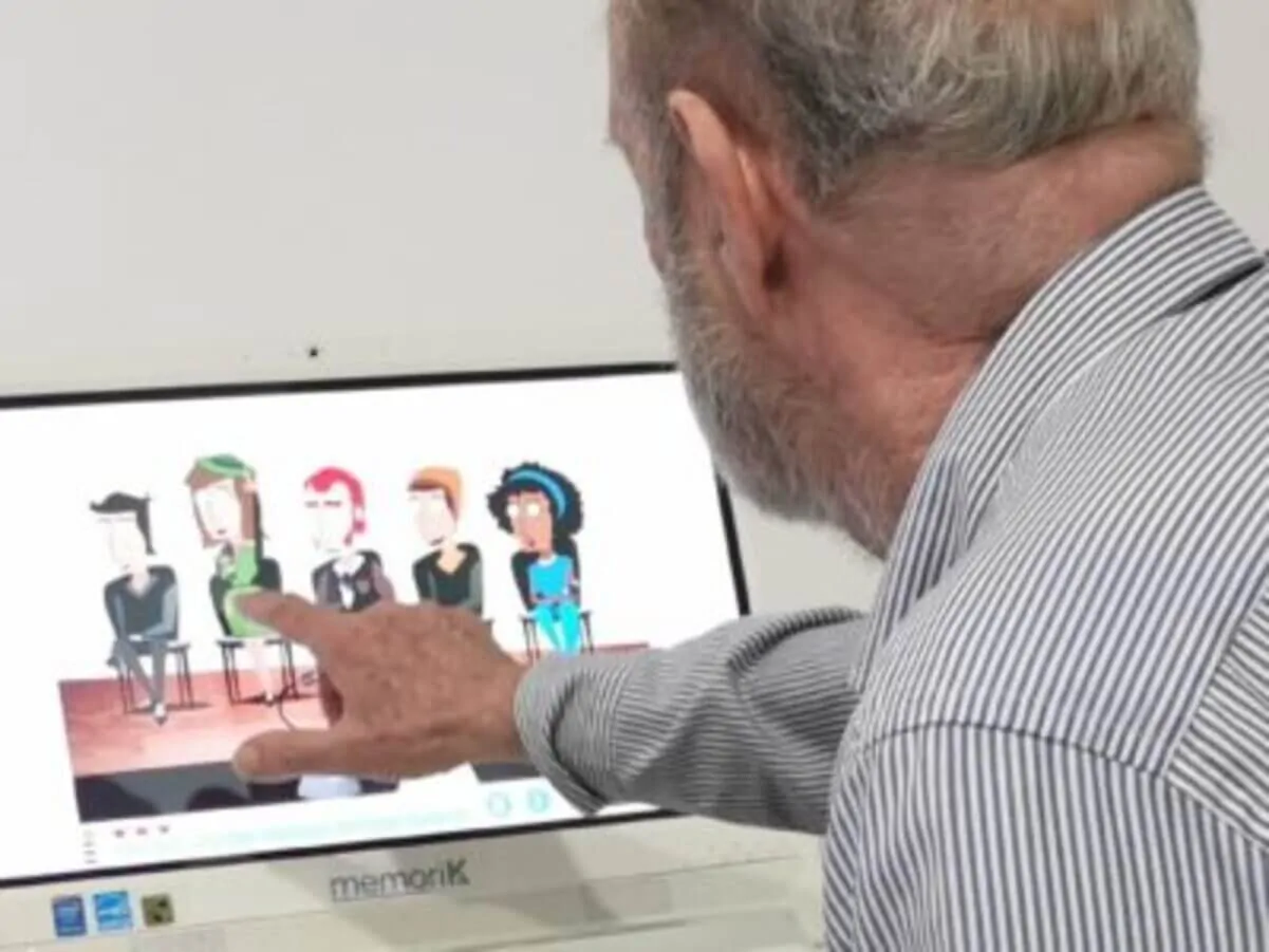 Idoso diante de um computador, apontando para uma ilustração com figuras na tela durante a estimulação cognitiva híbrida.