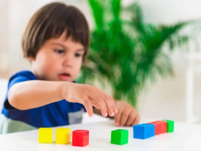 Criança pequena concentrada diante de uma mesa com blocos coloridos, avaliando habilidades visuoespaciais.