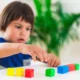 Criança pequena concentrada diante de uma mesa com blocos coloridos, avaliando habilidades visuoespaciais.