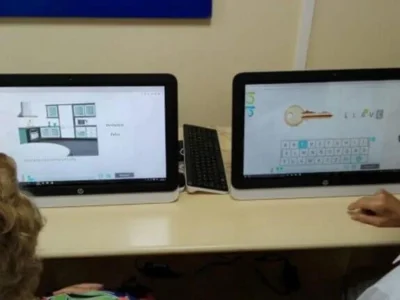 Dois computadores em uma mesa educativa; as telas mostram um layout de cozinha e uma tecla, com dois usuários em frente a elas.
