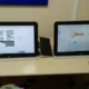 Dois computadores em uma mesa educativa; as telas mostram um layout de cozinha e uma tecla, com dois usuários em frente a elas.