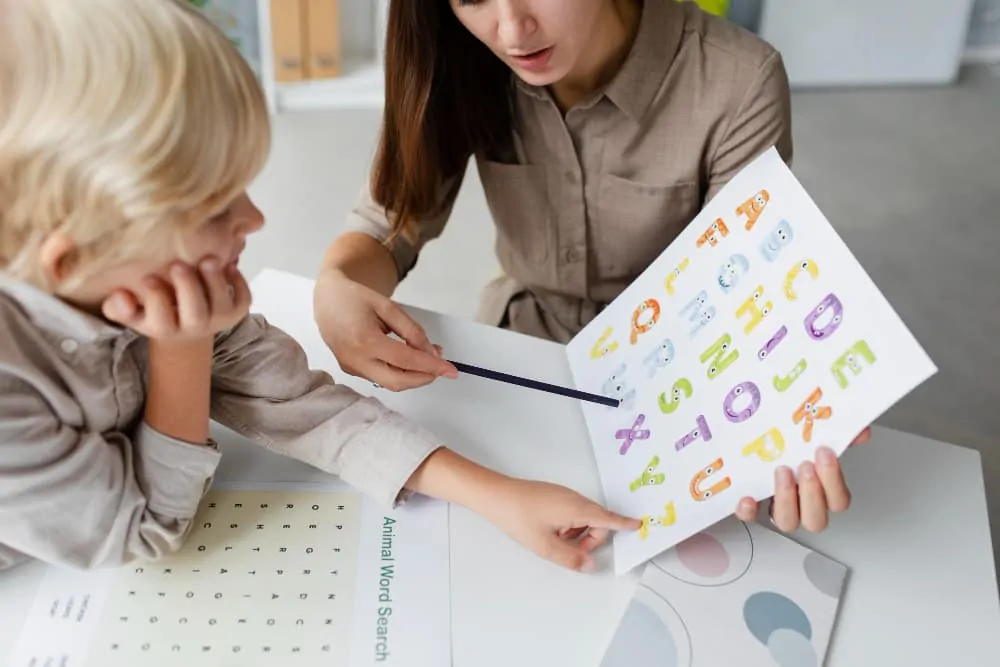 Sessão de fonoaudiologia em consulta clínica: fonoaudiólogo com uma criança trabalhando com cartões de letras coloridos na mesa.