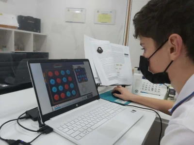 Jovem sentado em frente a um laptop com máscara, resolvendo um jogo de círculos na tela durante a atenção no TDAH.