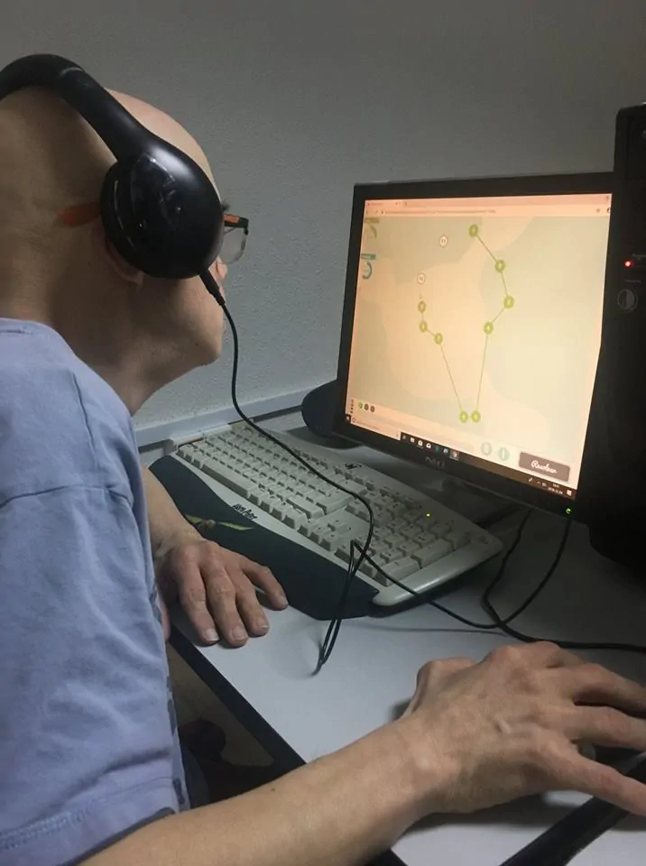 Persona con cabeza rapada y auriculares observa una pantalla, interactuando con una app de puntos conectados.
