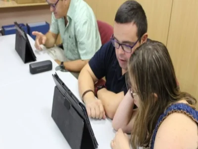 Três pessoas ao redor de uma mesa observam um tablet durante uma sessão de estimulação cognitiva, no ambiente da FUNDOWN.