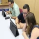 Três pessoas ao redor de uma mesa observam um tablet durante uma sessão de estimulação cognitiva, no ambiente da FUNDOWN.