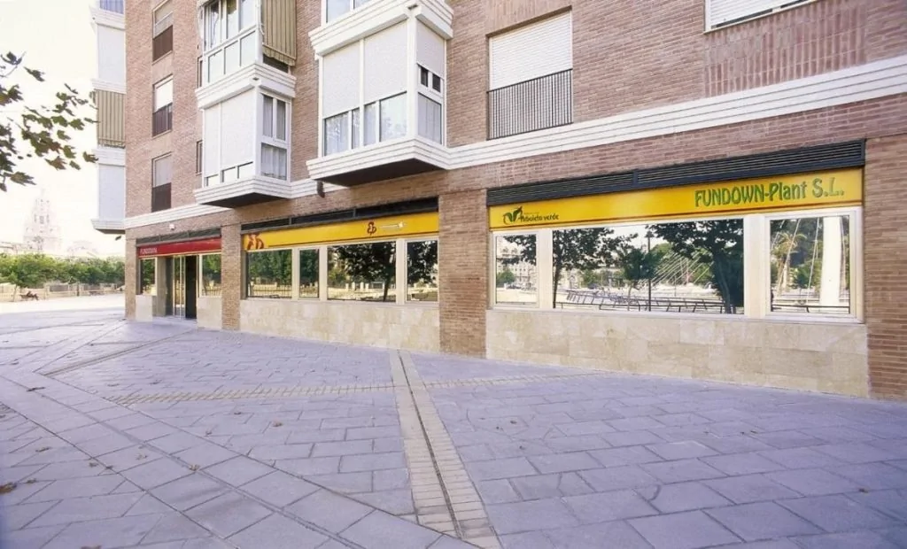 Fachada de un edificio urbano de varios pisos con escaparates y un rótulo FUNDOWN-Plant S.L. en la planta baja, entorno urbano.