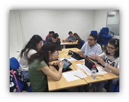 Grupo de estudiantes alrededor de una mesa en aula, usando tablets durante una sesión de estimulación cognitiva de FUNDOWN.