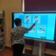 Criança sentada em frente a um tablet, realizando exercícios de cognição social com o NeuronUP, supervisionada por um profissional.