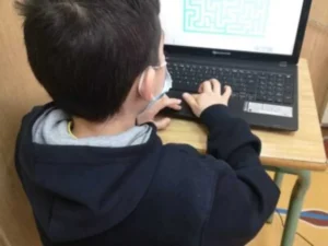 Aluno em sala de aula, sentado diante de um notebook com máscara, concentrado em um labirinto na tela para estimulação cognitiva com o NeuronUP.