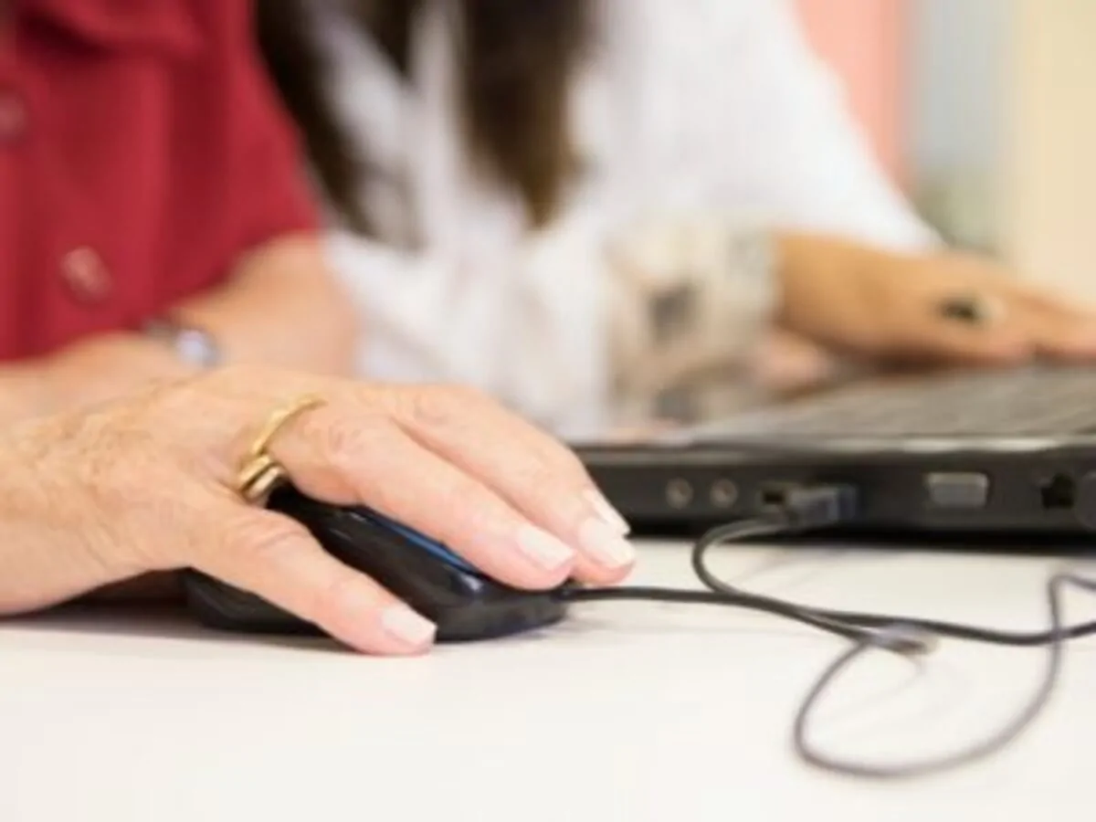 Mão de pessoa idosa usando mouse; ao fundo, outra mão com teclado, em um aprendizado centrado na estimulação cognitiva.