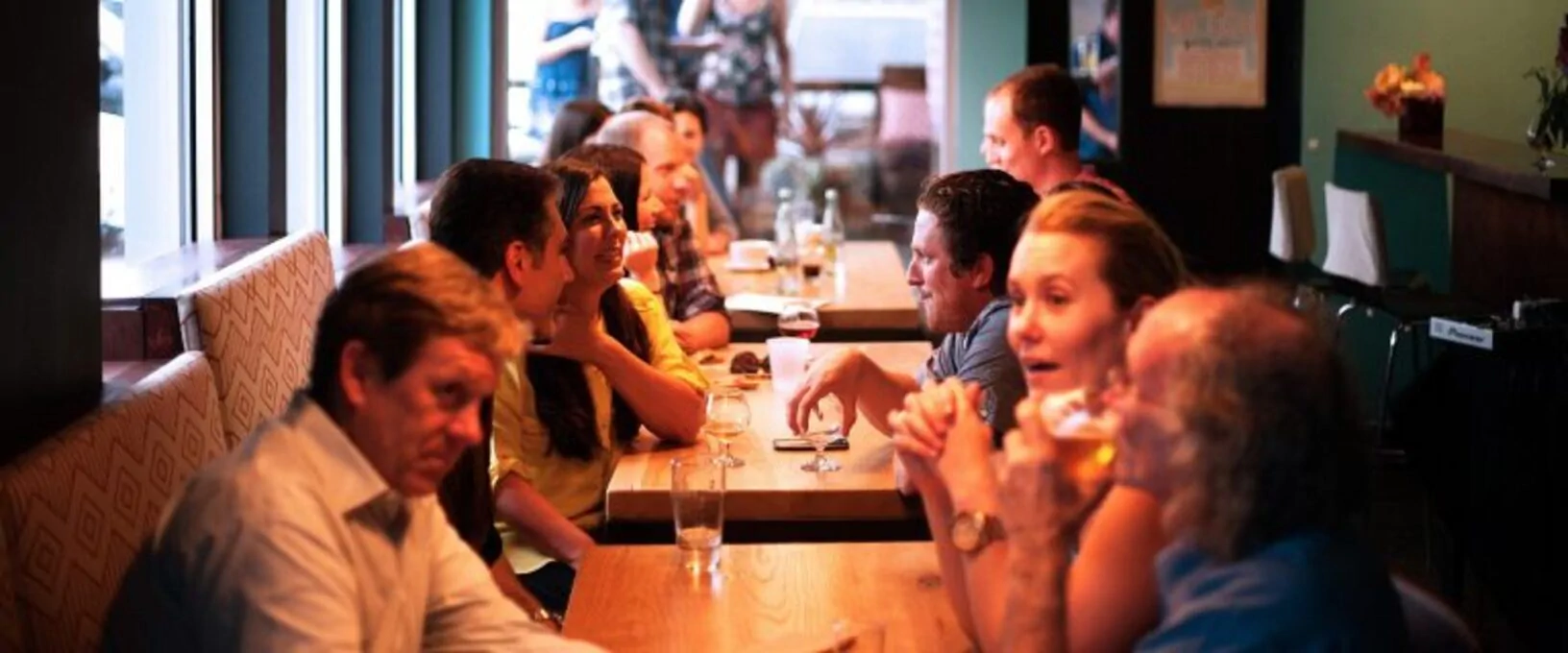 Grupo diverso de pessoas sorrindo e conversando em um ambiente acolhedor, tipo café, uma atividade de habilidades sociais.