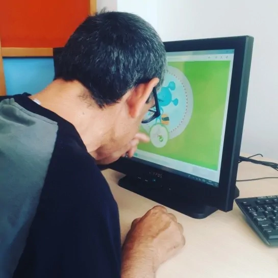 Pessoa sentada em frente a um computador, interagindo com uma interface colorida de fundo verde e um personagem azul.