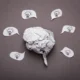 Bola de papel amassado em forma de cérebro, rodeada por balões de diálogo com lâmpadas sobre fundo cinza.
