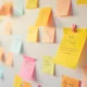 Parede coberta de notas adesivas coloridas (amarelo, rosa e laranja) para organizar ideias e tarefas, com uma nota em destaque que parece dizer 'Tilly's Menu'.