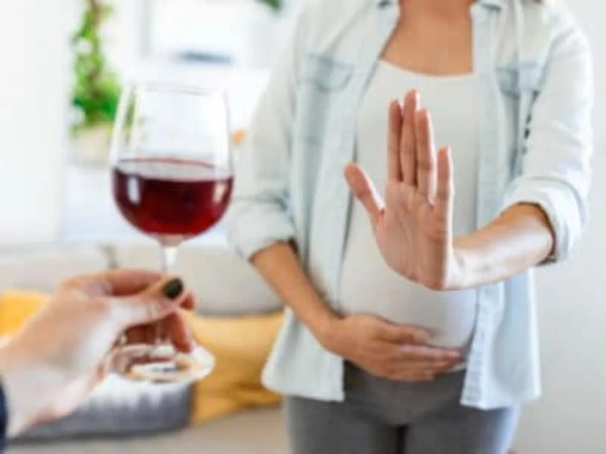 Mulher grávida recusando uma taça de vinho em um ambiente doméstico, destacando a prevenção do álcool durante a gravidez.