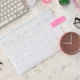 Plano cenital de mesa de trabalho organizada com calendário, relógio rosa, laptop, óculos e planta, com foco na gestão do tempo.