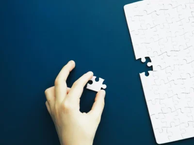 Mão colocando uma peça de quebra-cabeça sobre um tabuleiro azul, contexto de desenvolvimento cognitivo e autismo.