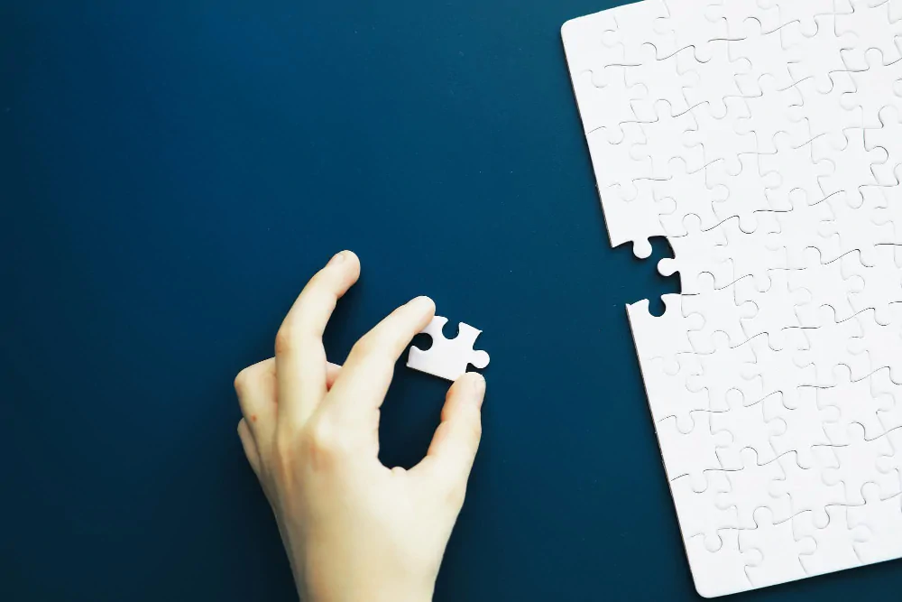 Mão colocando uma peça de quebra-cabeça sobre um tabuleiro azul, contexto de desenvolvimento cognitivo e autismo.
