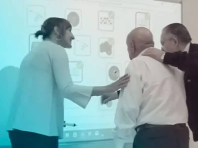 Grupo de três idosos interagindo em uma sessão de estimulação cognitiva com cartões de exercícios diante de uma tela.