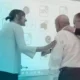 Grupo de três idosos interagindo em uma sessão de estimulação cognitiva com cartões de exercícios diante de uma tela.