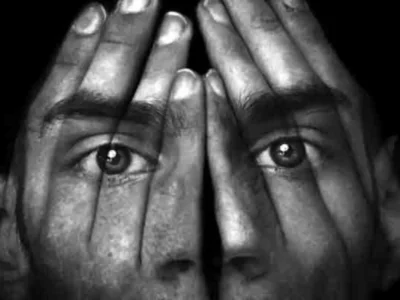 Composição em preto e branco: duas faces entrelaçadas por mãos que cobrem os rostos, olhos alinhados, efeito surreal.