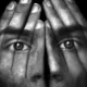 Composição em preto e branco: duas faces entrelaçadas por mãos que cobrem os rostos, olhos alinhados, efeito surreal.