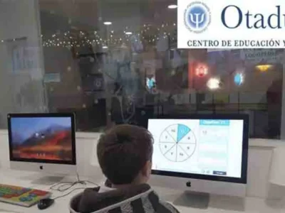 Criança em frente a um computador com dois monitores, um com gráfico circular; fundo com Otaduy Centro de Educação e Saúde.
