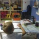 Menino sentado diante de um tablet e de uma folha sobre uma mesa branca, dentro de uma sala de aula organizada para exercícios de estimulação neuropsicológica da dislexia.