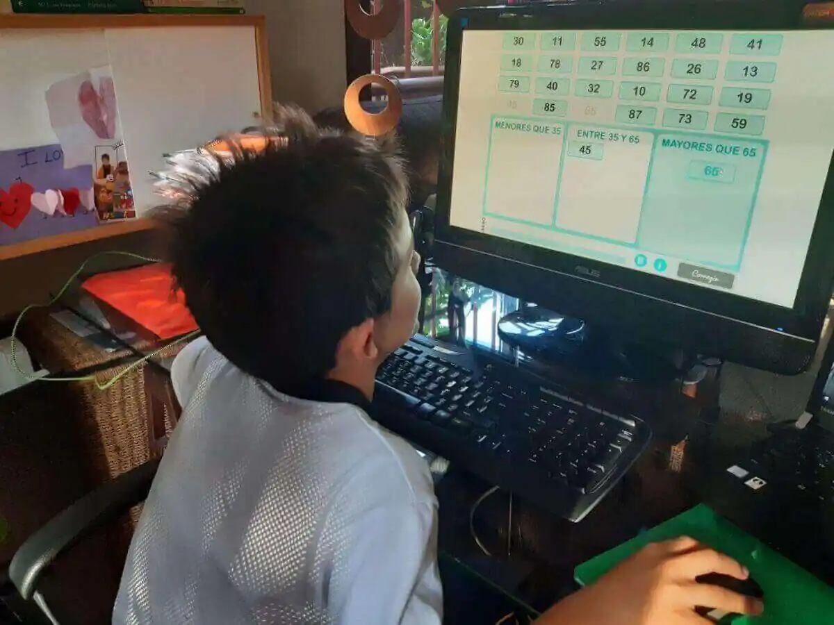 Criança sentada em frente a um computador observa uma atividade educativa com números na tela, em um ambiente de estudo.