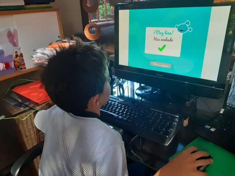Criança em frente a um computador em um ambiente de estudo, tela com uma mensagem de sucesso após completar um exercício.