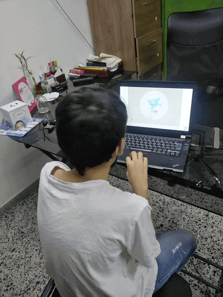 Criança sentada em frente a um laptop, realizando exercícios de reabilitação e estimulação cognitiva com tecnologia.