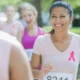 Grupo de mulheres correndo em uma corrida ao ar livre, com camisetas cor-de-rosa e dorsais, em um ambiente verde.
