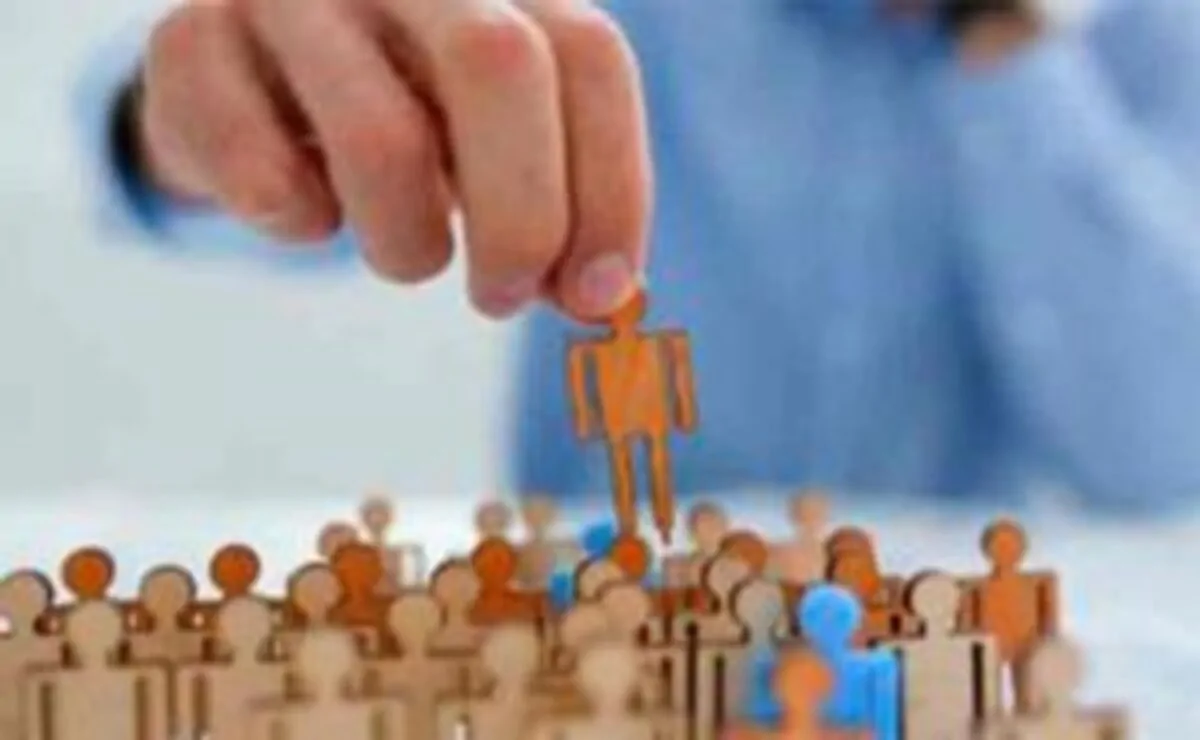 Mão segurando uma figura laranja sobre um grupo de figuras bege e azuis, todas em estilo de silhuetas simples.