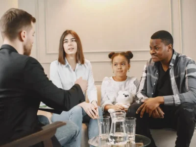 Grupo diverso de famílias e profissionais sentados em círculo ao redor de uma criança, compartilhando apoio ao neurodesenvolvimento.