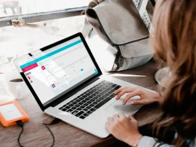 Pessoa em frente a um laptop em uma mesa de madeira; xícara de café e um disco rígido, ambiente para terapia ocupacional em casa.