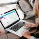 Pessoa em frente a um laptop em uma mesa de madeira; xícara de café e um disco rígido, ambiente para terapia ocupacional em casa.