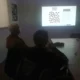 Duas pessoas sentadas olham para um projetor que mostra um gráfico de formas e números, com corações, em uma sala de reuniões.
