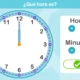 Relógio analógico com ponteiros em 12 e 6, botões de ajuste e verificação, fundo azul, pergunta: Que horas são?