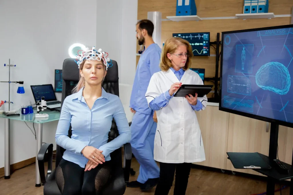 Mulher com dispositivo EEG na cabeça, em um laboratório médico com tablet e monitor de dados neurais.