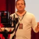 Fotografia de Jesús M. Cortes em uma intervenção pública, com microfone e tela; ilustra a entrevista sobre a previsão da deterioração cognitiva com NeuronUP.